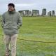 Person standing in front of a Stonehenge - large rocks in a field, organized in a circle 